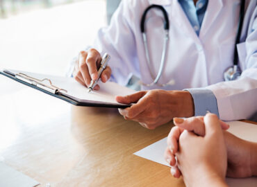 Patient listening intently to a male doctor explaining patient symptoms or asking a question as they discuss paperwork together in a consultation